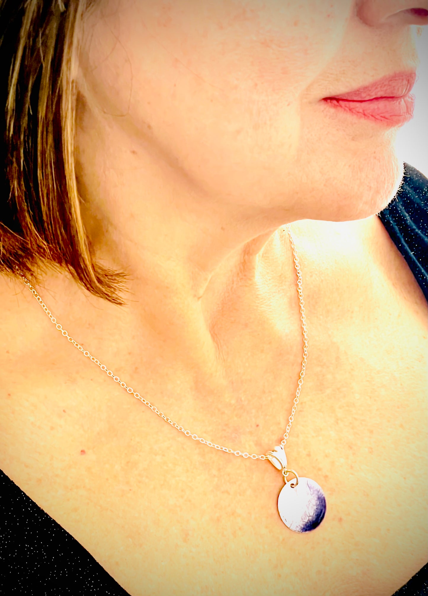 Woman wearing a gold chain necklace with a round, iridescent purple and white pendant.