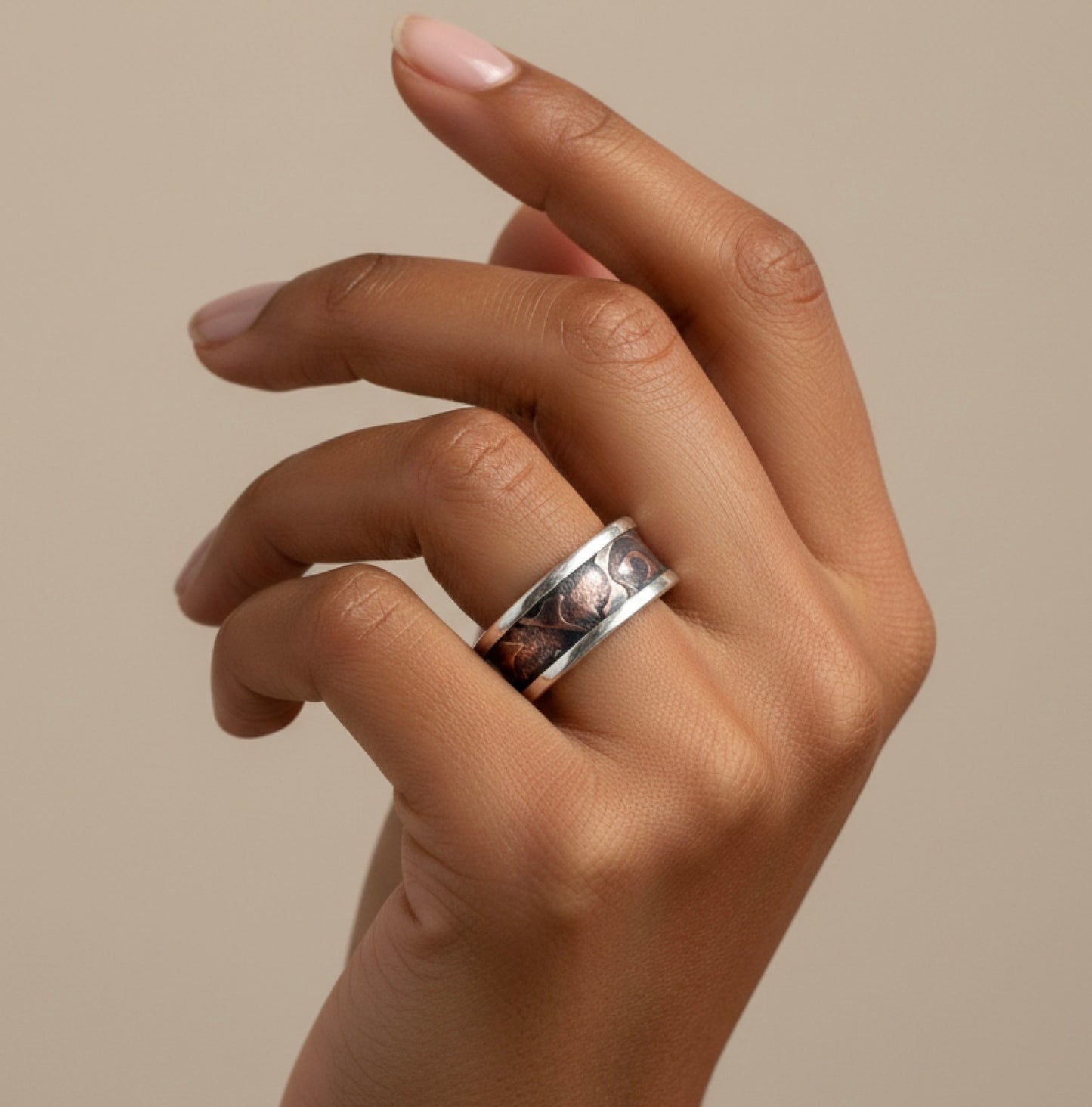 Hand wearing a silver ring with intricate design on a beige background