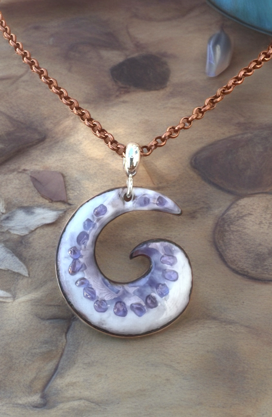 Crescent moon-shaped pendant on a chain against a natural stone background