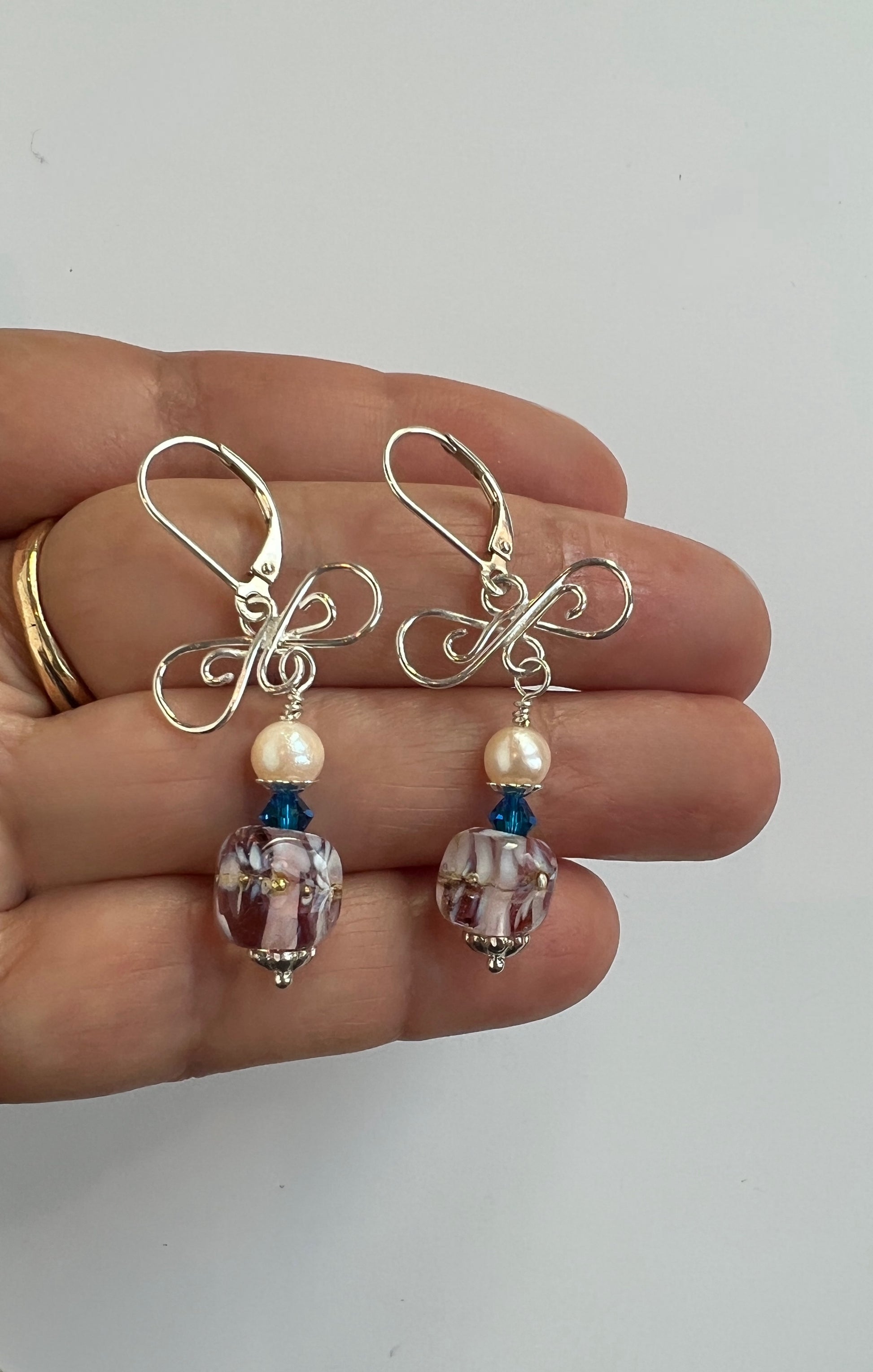 Pair of earrings with beads held between fingers on a light background