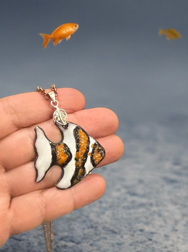Hand holding a fish-shaped pendant with fish in the background, clown fish