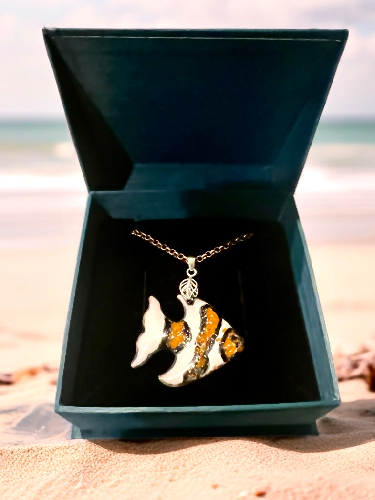 Fish-shaped pendant necklace in a jewelry box on a beach, clown fish