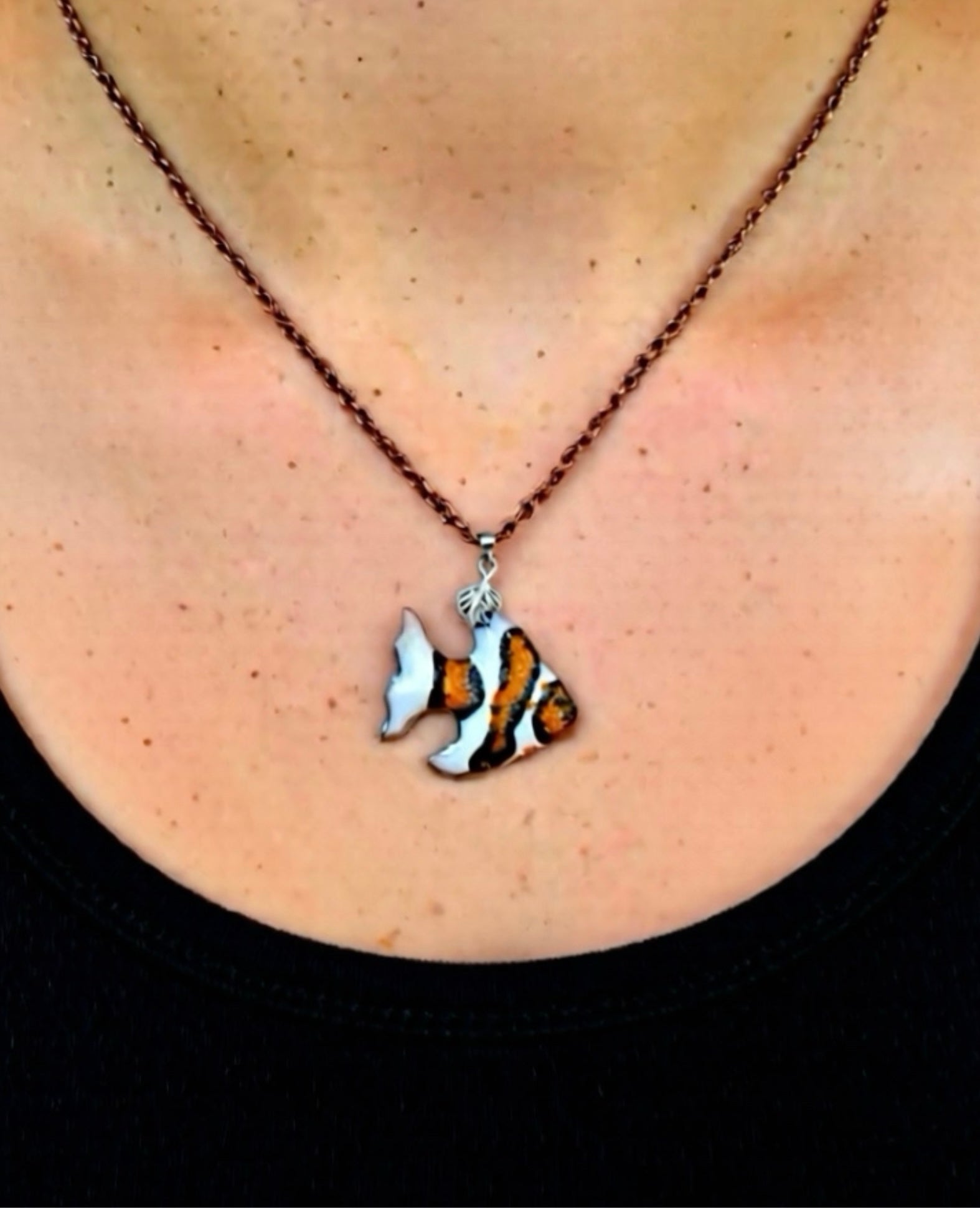 Necklace with a fish pendant worn by a person. Fish is clown fish stripped in orange, white and black. Copper chain 18 inches