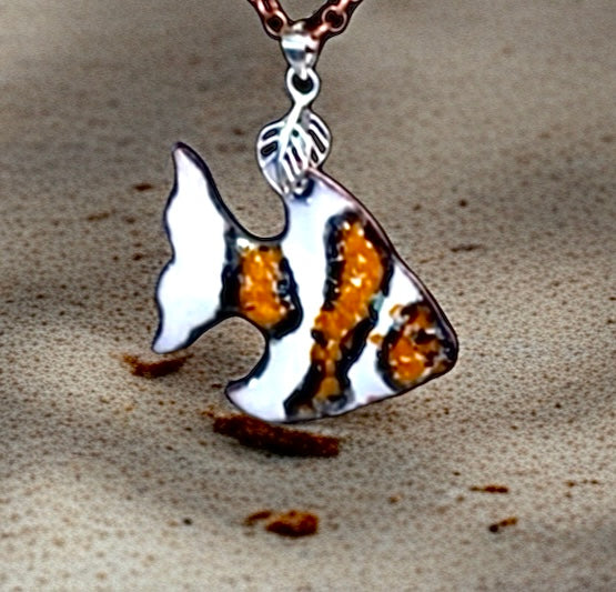Fish-shaped pendant on a chain against a textured beige background, clown fish