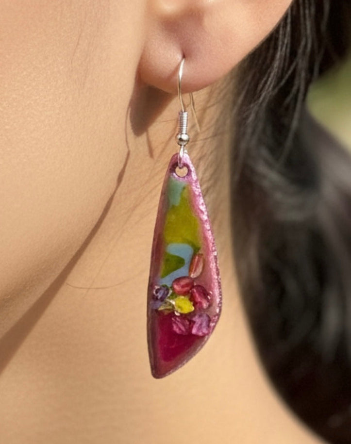 Colorful teardrop-shaped earring on a blurred background, green and pink