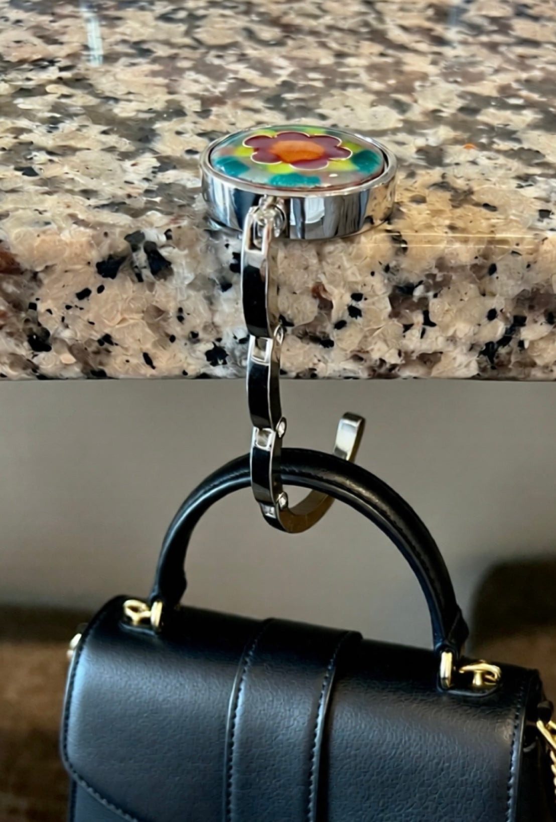 Black handbag with a floral hook on a marble countertop