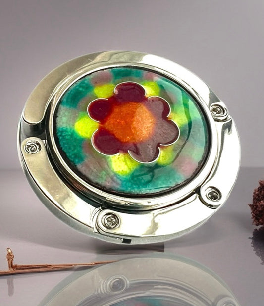 Round metal purse hanger hook with a colorful floral design on a reflective surface