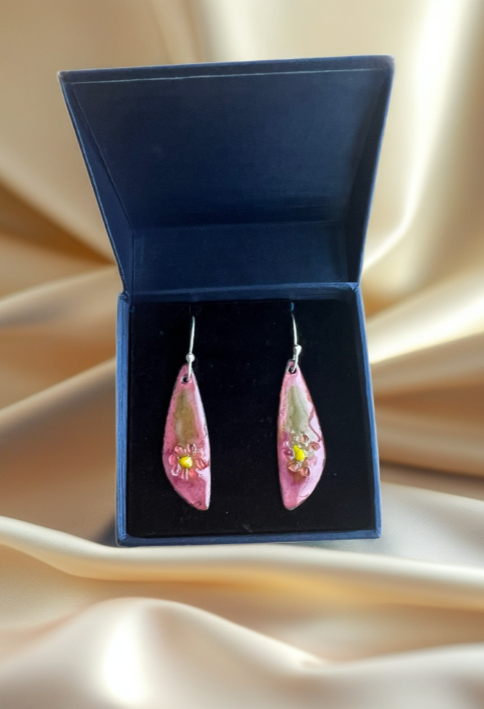 Pink teardrop earrings in a blue jewelry box on a beige fabric background