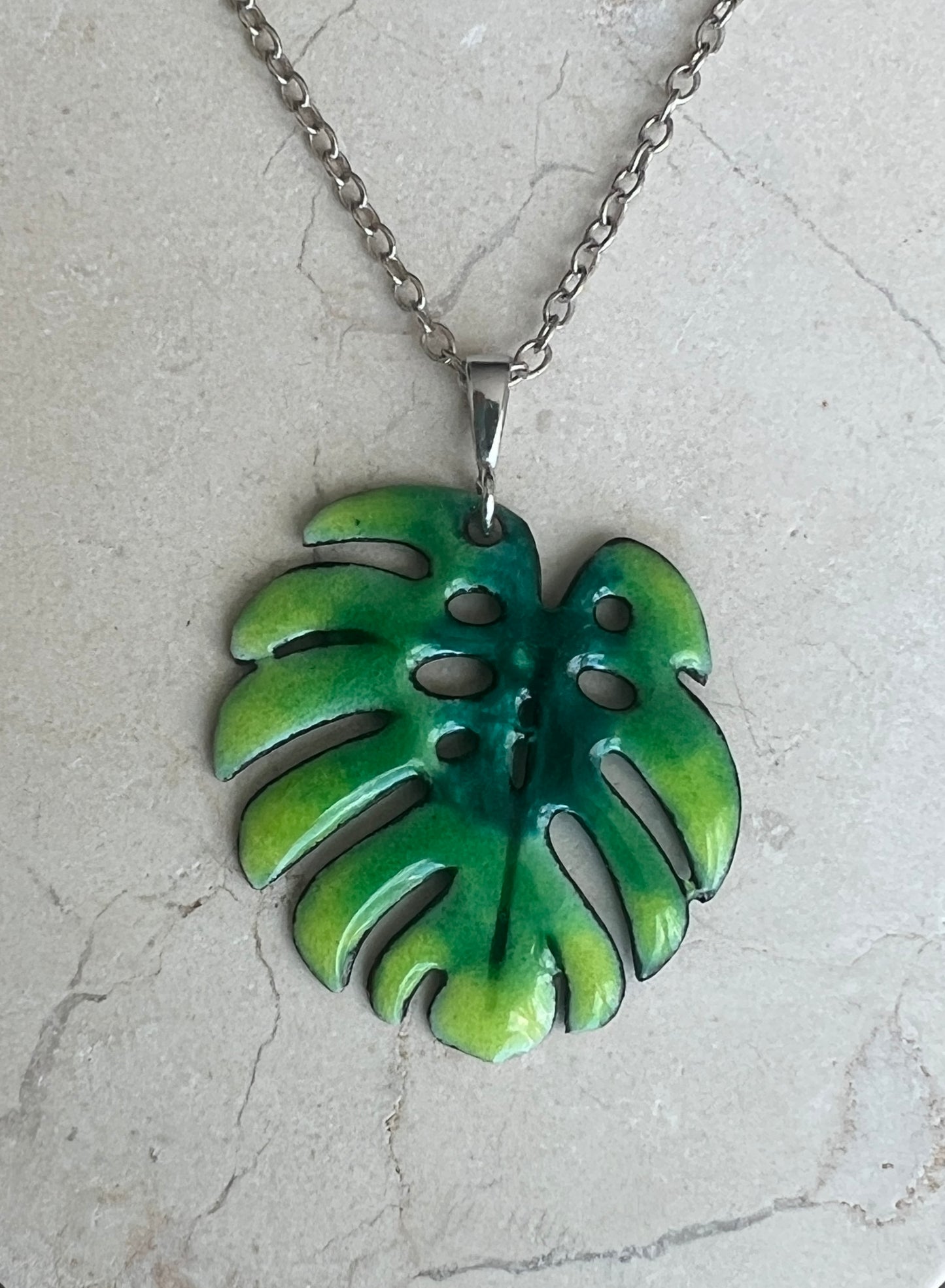 Green leaf-shaped pendant on a chain against a light gray background, Monstera leaf, Silver Chain