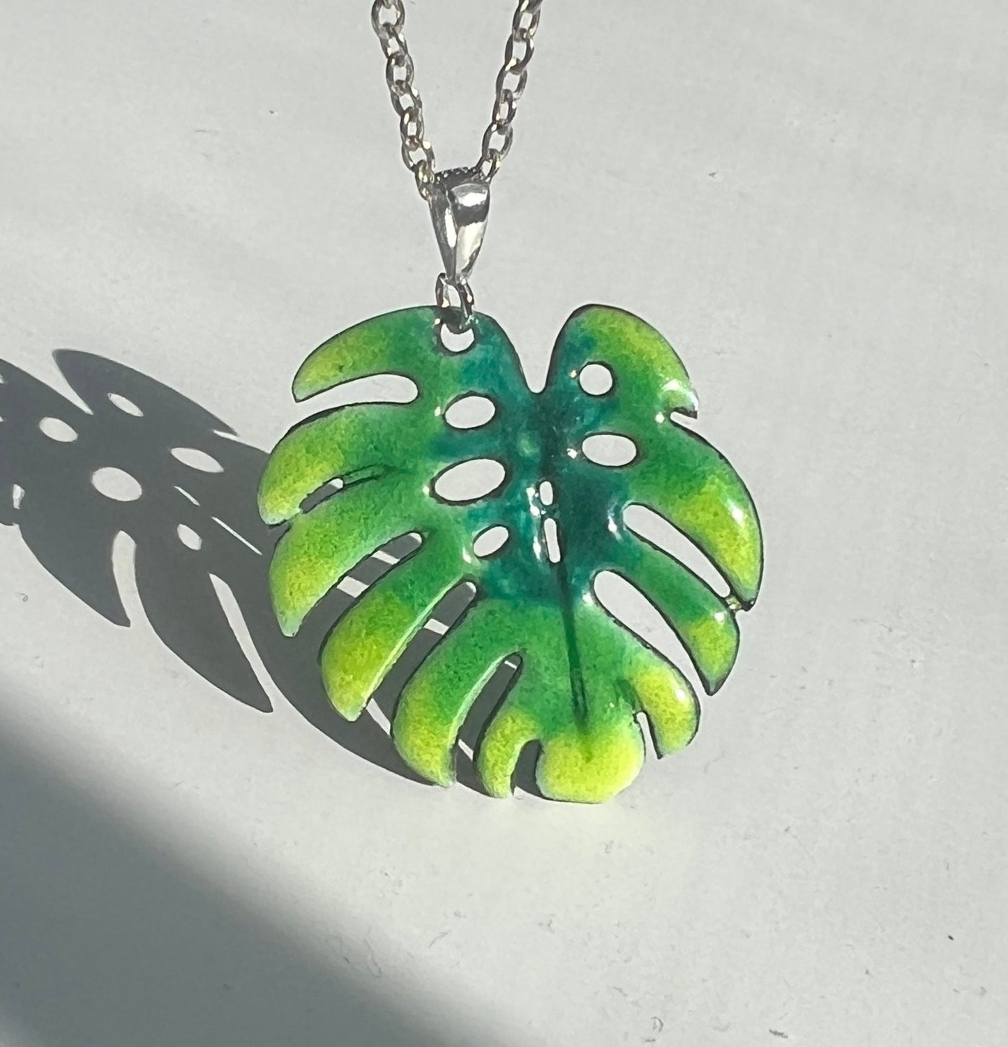 Green leaf-shaped pendant on a chain against a light background. Silver chain