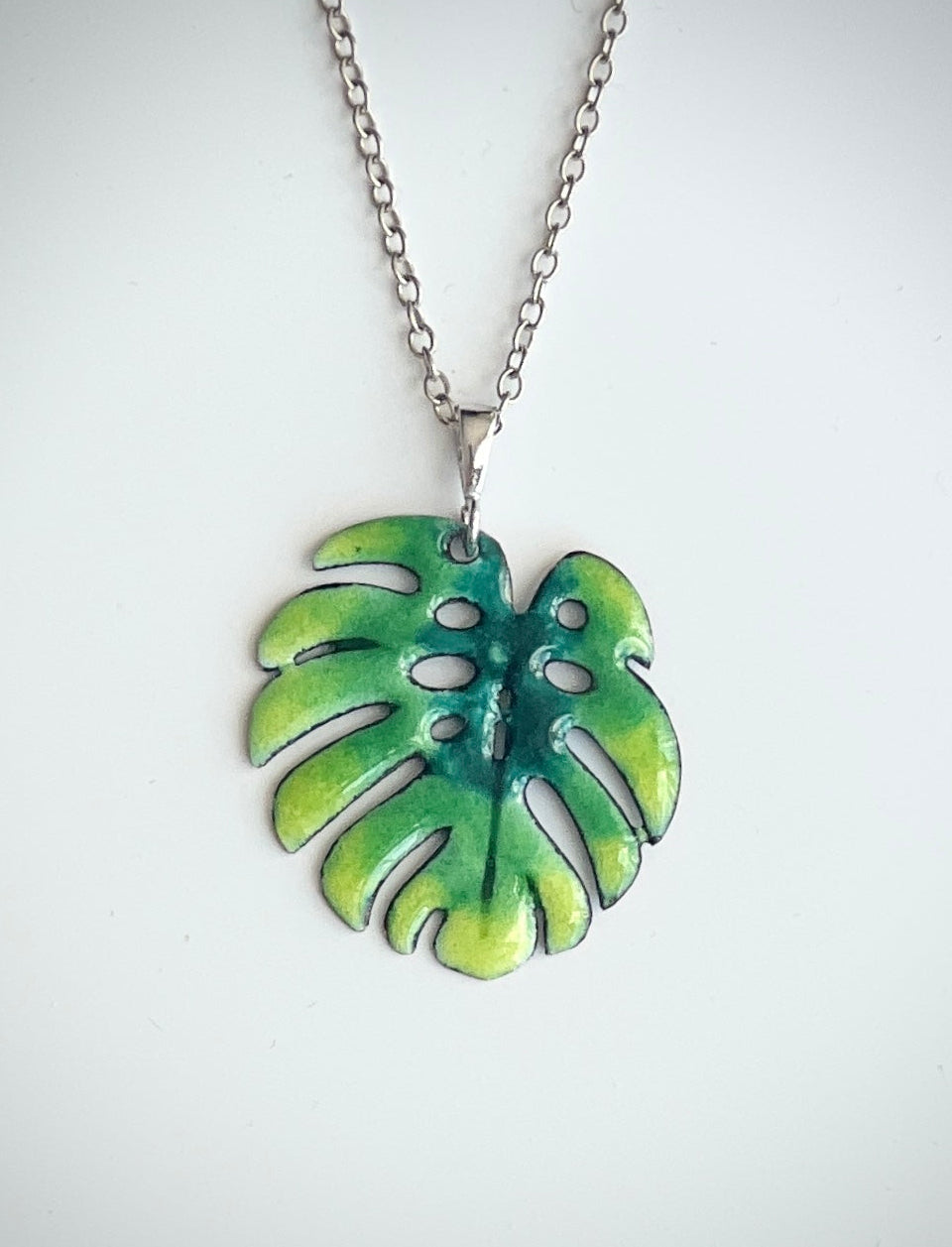 Green leaf-shaped pendant on a chain against a white background, Monstera leaf