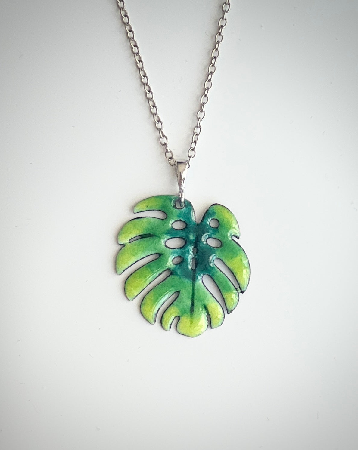 Green leaf-shaped pendant on a silver chain against a white background. Monstera Leaf