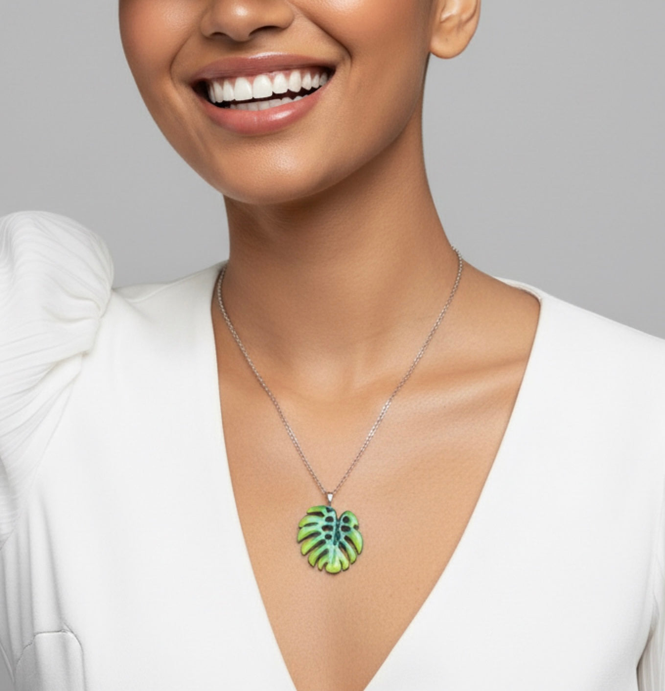 Woman wearing a necklace with a green pendant against a gray background. Monstera leaf