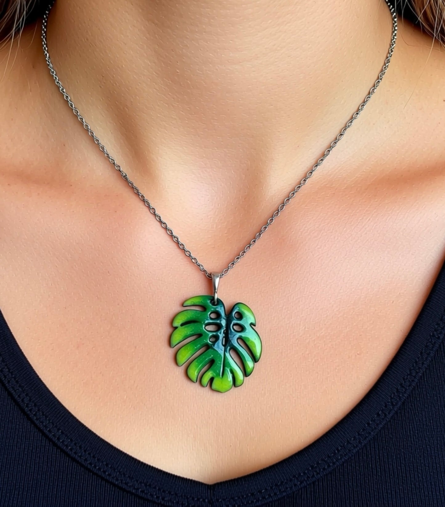 Green leaf-shaped pendant on a necklace against a neutral background, Monstera leaf
