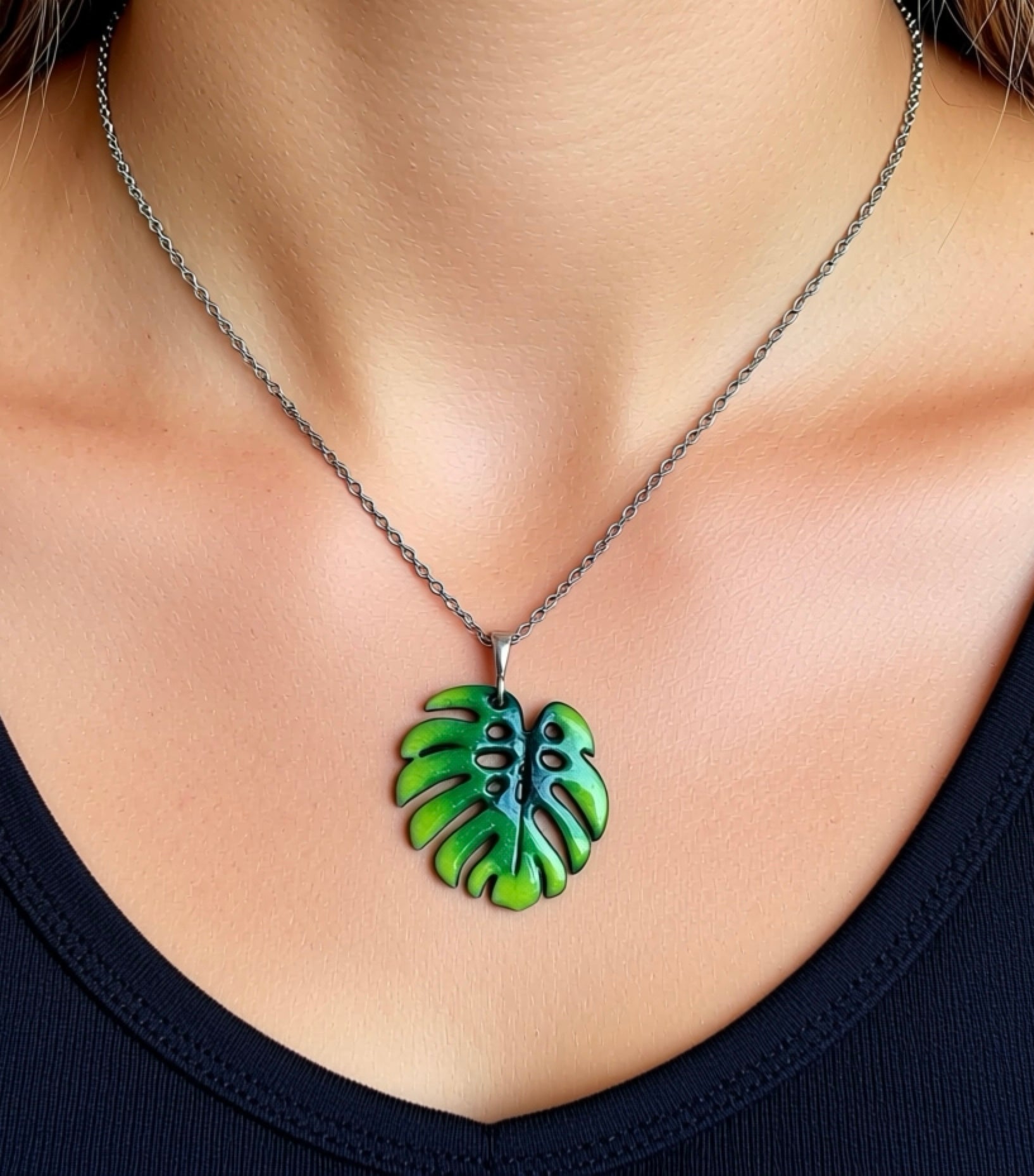 Green leaf-shaped pendant on a necklace against a neutral background, Monstera leaf