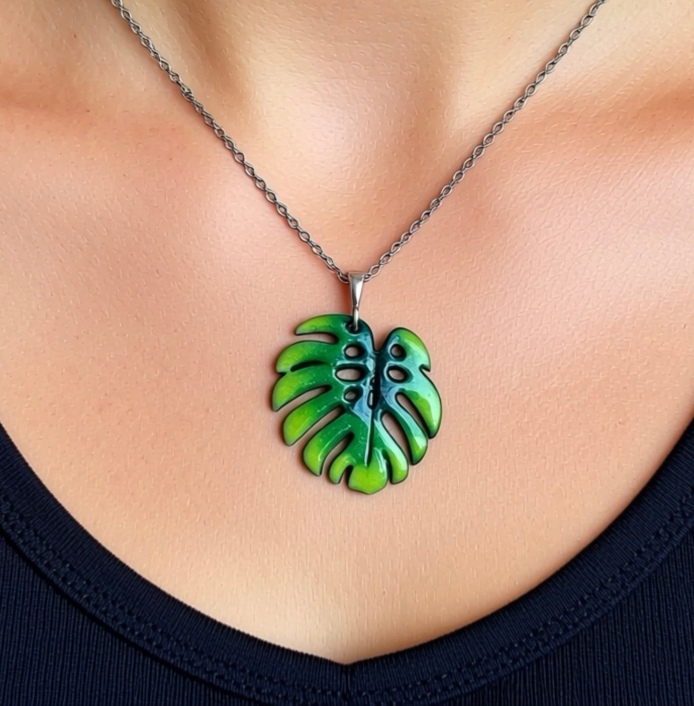 Green leaf-shaped pendant on a chain worn around the neck. Silver chain