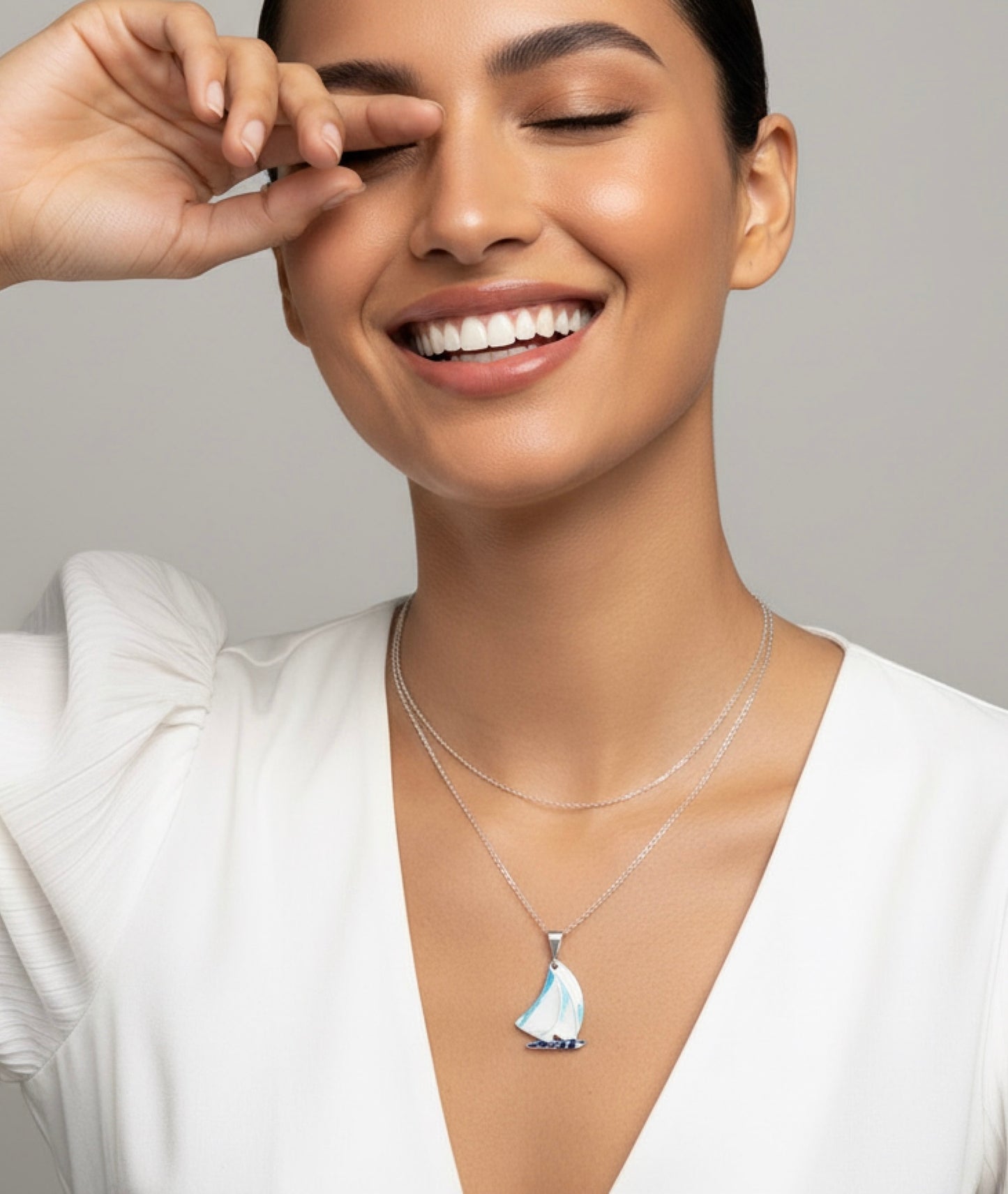 Woman wearing a necklace with a sailboat pendant against a neutral background