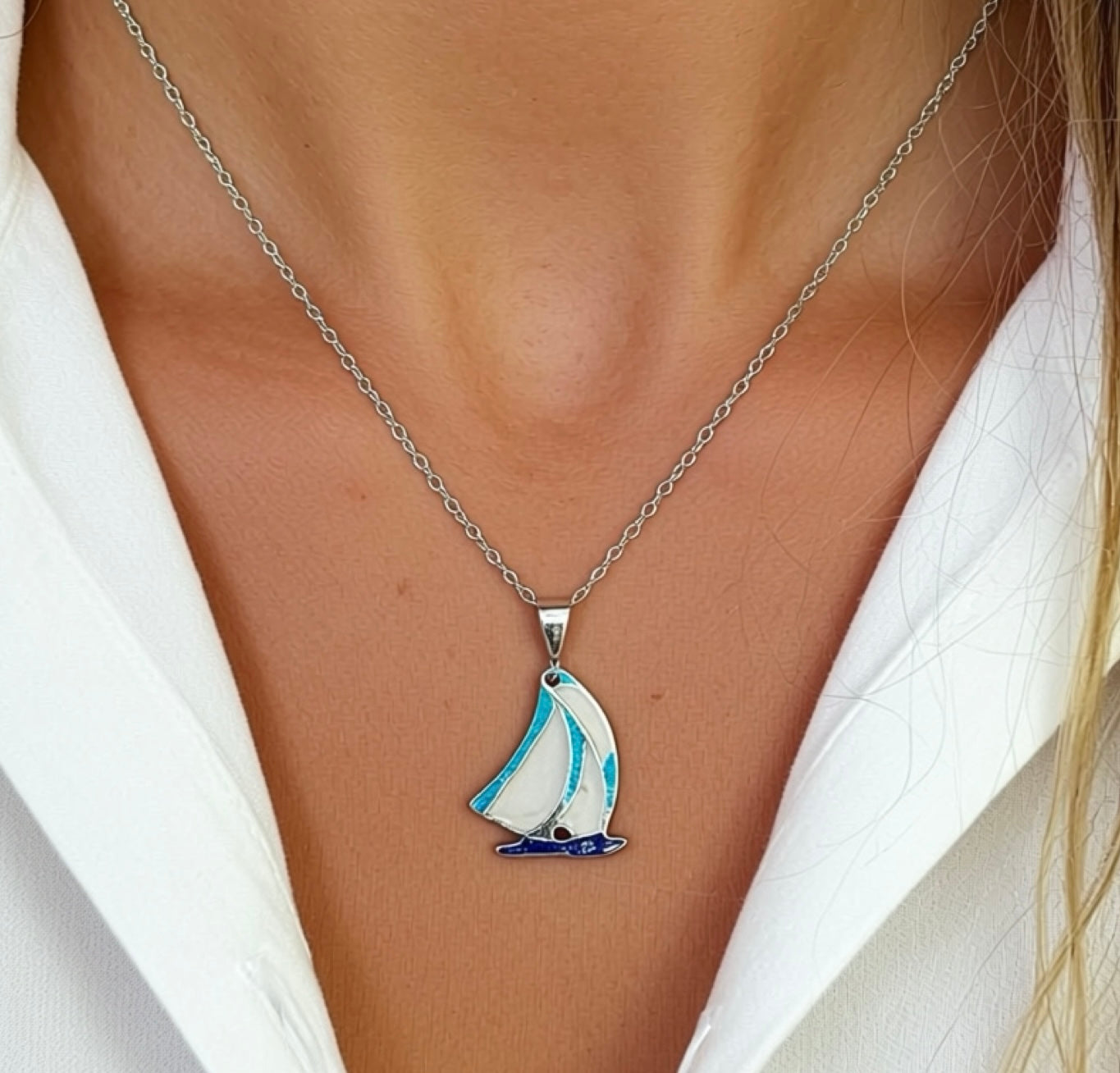 Sailboat pendant necklace on a person wearing a white shirt
