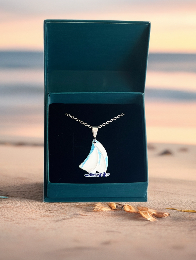 Necklace with sailboat pendant in a teal box on a beach