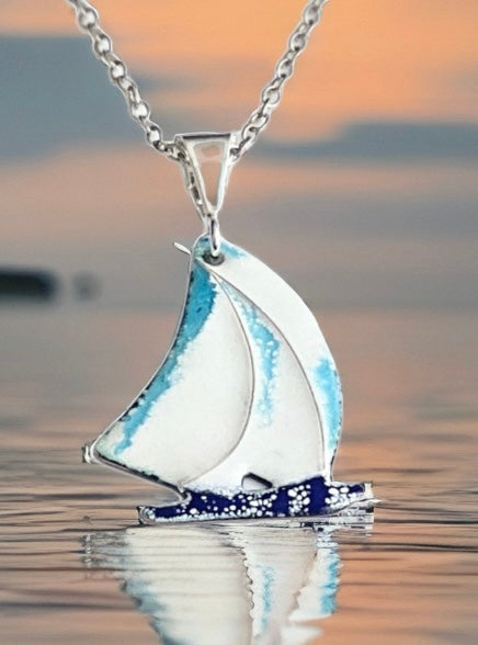 Silver sailboat pendant with blue accents on a blurred water background