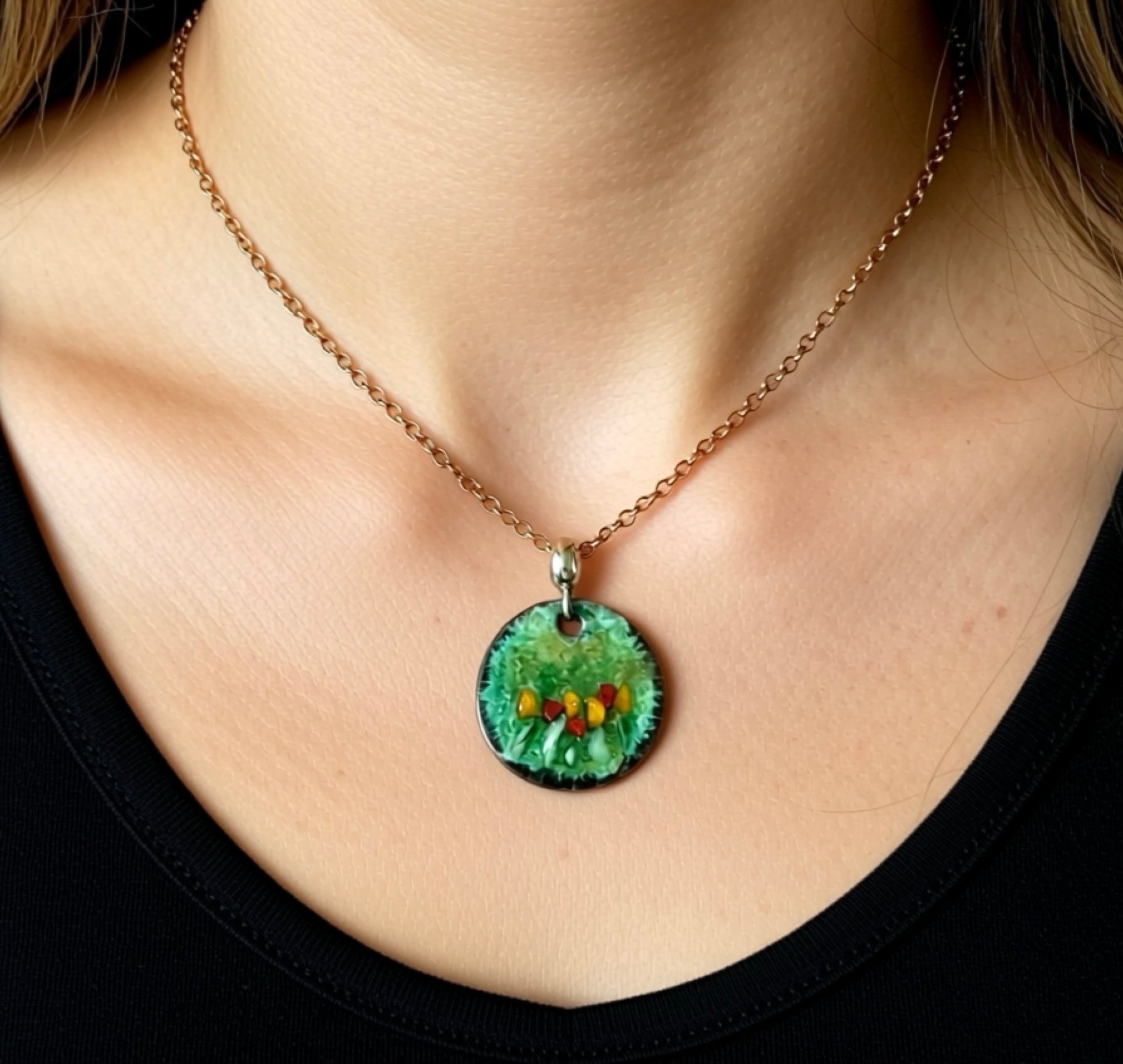 Necklace with a green pendant featuring small colorful stones worn by a person.
