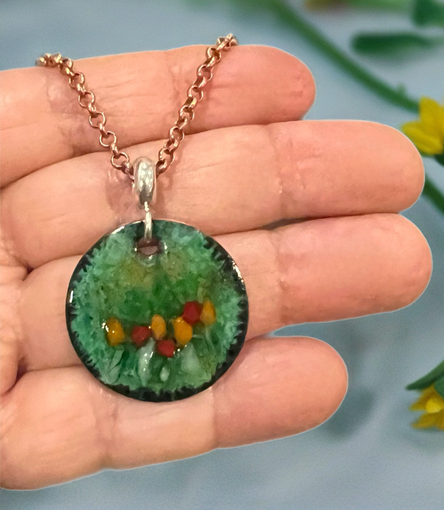 Necklace with a round pendant featuring colorful fish on a hand against a blurred natural background