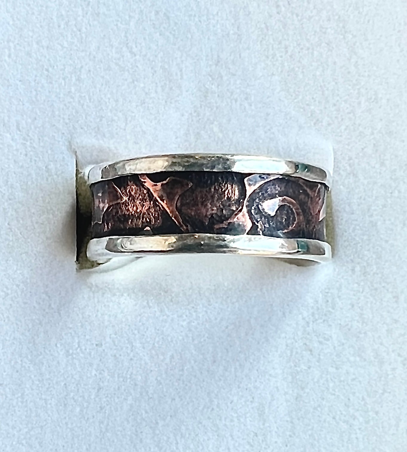 Silver ring with textured design on a light gray background