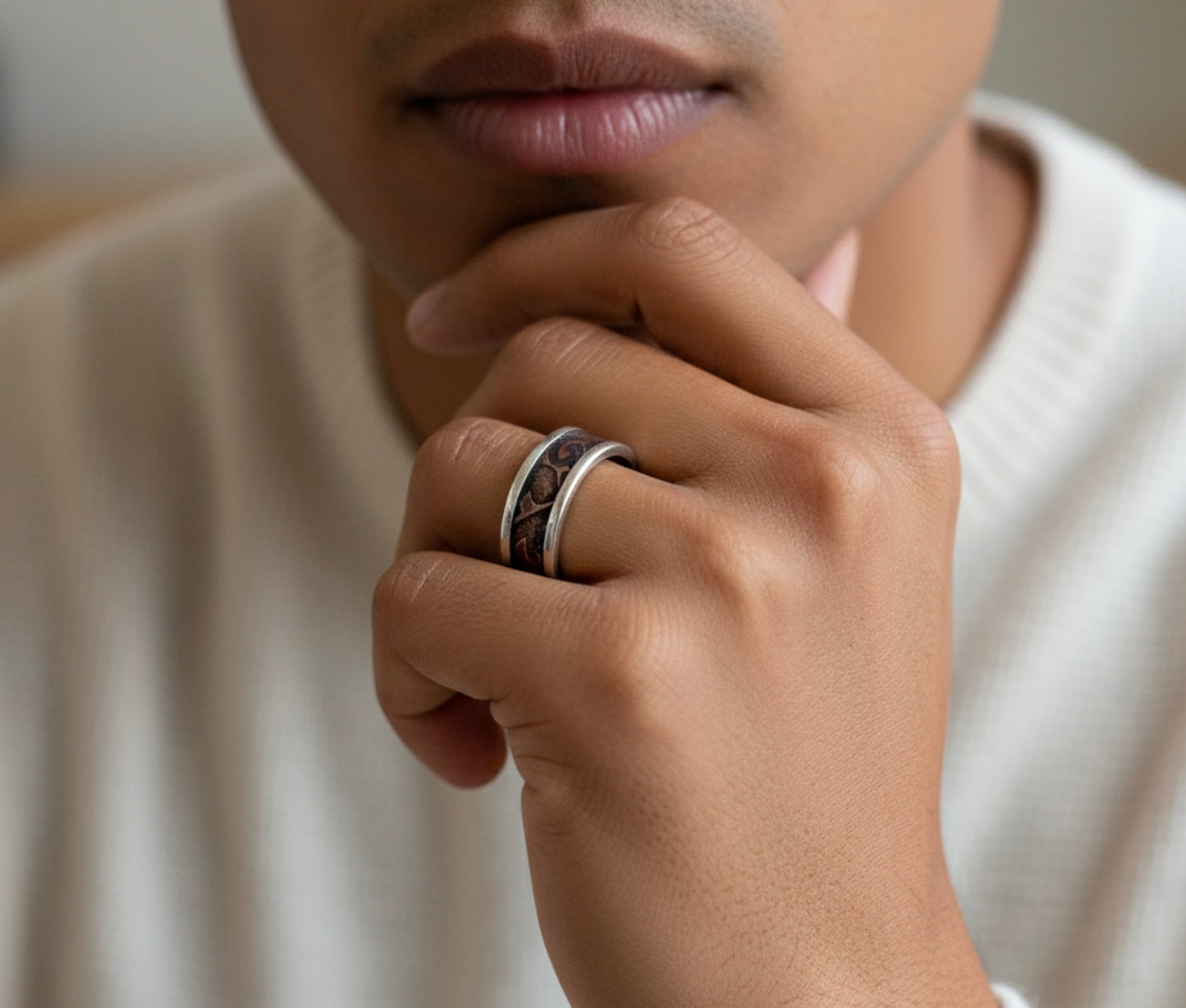 Close-up of a hand wearing a silver ring with a dark stone, resting on the chin.
