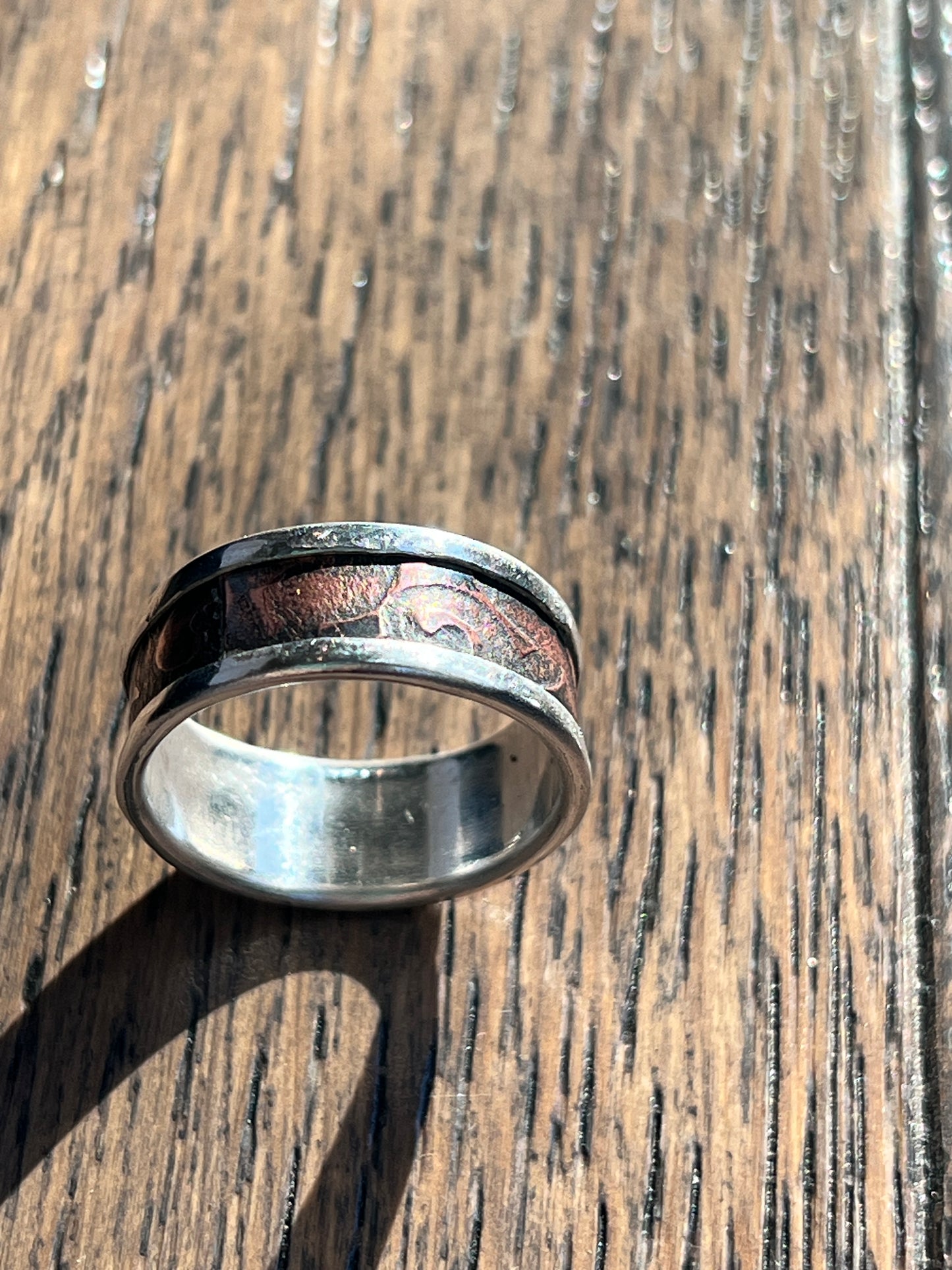 Silver ring with a textured band on a wooden surface