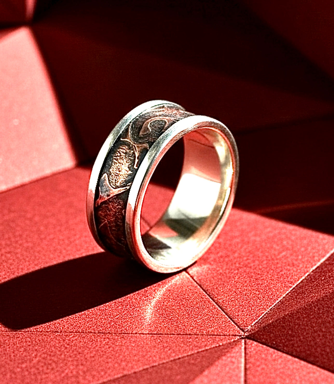 Silver ring with intricate design on a red geometric background