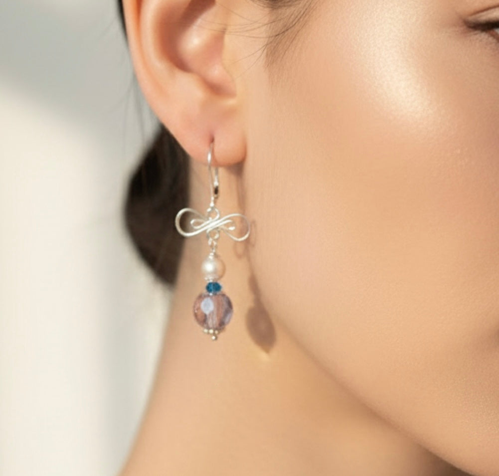 Close-up of an ear wearing a silver earring with a pearl and gemstone bead.