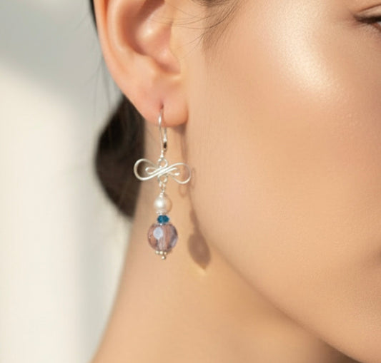 Close-up of an ear wearing a silver earring with a pearl and gemstone bead.