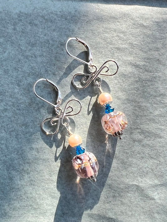 Butterfly-shaped earrings with pink and blue beads on a gray surface