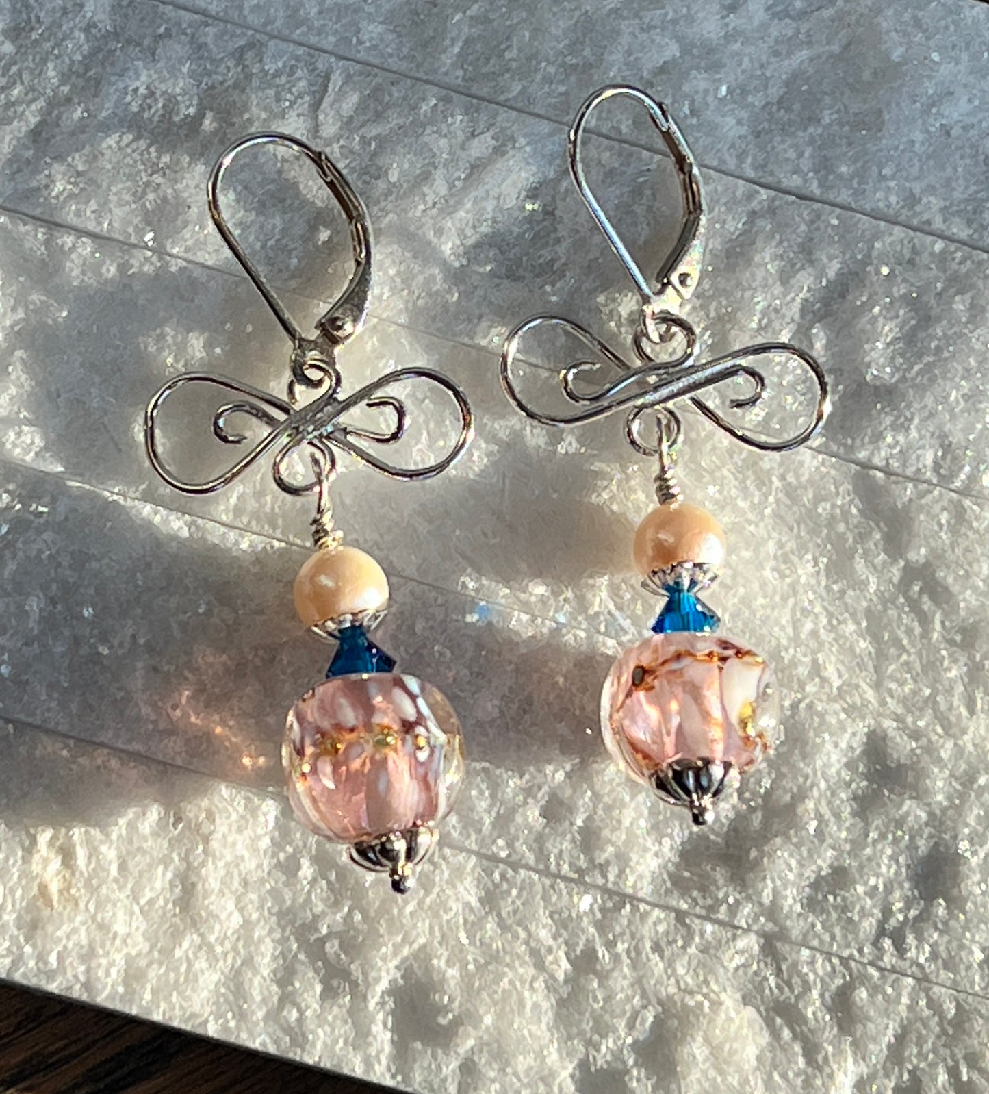 Pair of earrings with pink beads and silver hooks on a textured surface