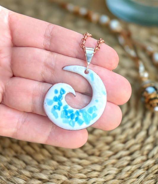 Hand holding a crescent moon-shaped pendant with blue and white design on a woven mat background