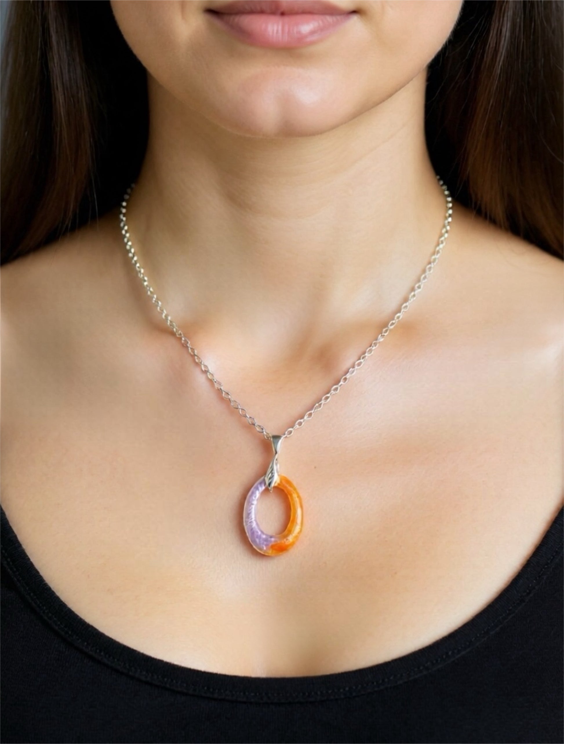 Close-up of a necklace with a colorful pendant on a person wearing a black top.