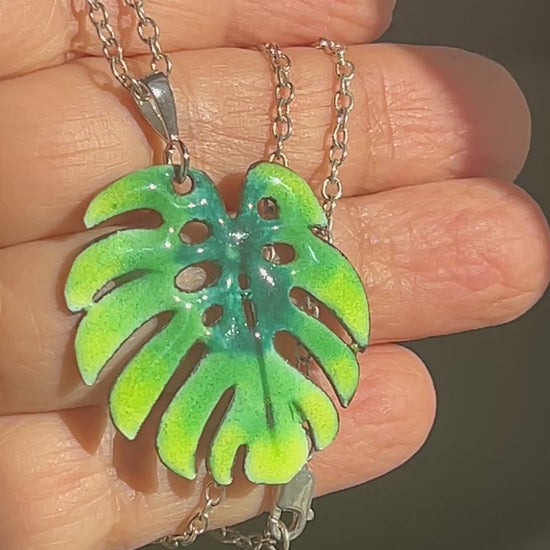 Hand holding green enamel monstera leaf pendant.