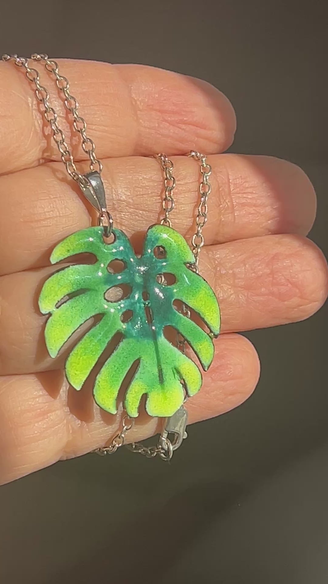 Hand holding green enamel monstera leaf pendant.
