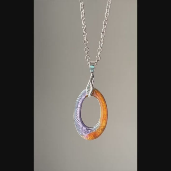 Purple and orange enamel silver pendant hanging from silver chain on a neutral color background