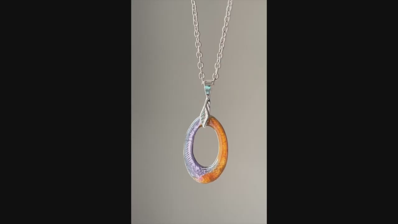 Purple and orange enamel silver pendant hanging from silver chain on a neutral color background