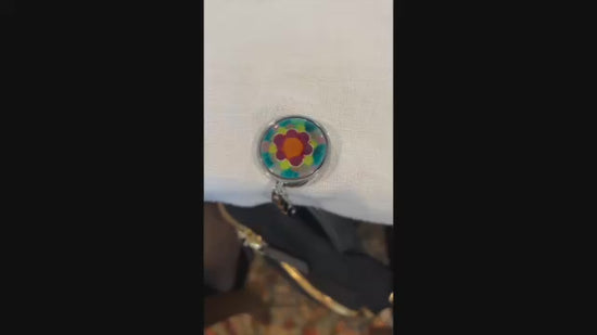 Video showing a black backpack hanging at a table from an enamel decorated hadbag hanger